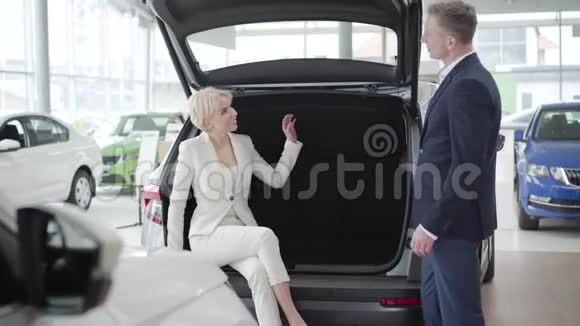 优雅的金发白种人女人坐在汽车后备箱里和经销商的商人交谈成功的年轻女商人视频的预览图