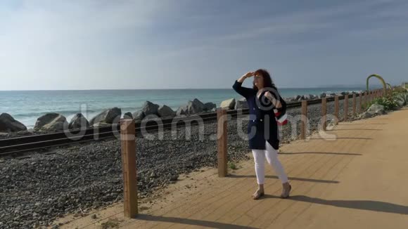 女人快乐美丽阳光明媚夏日散步远望海洋海岸旅游度假退休生活视频的预览图
