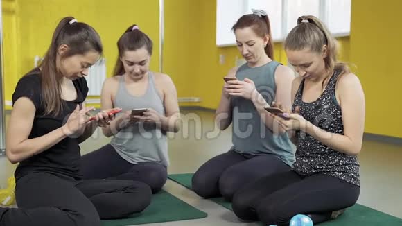 一群积极使用手机的年轻女性四个女孩坐在垫子上全神贯注地看着工作室里的智能手机视频的预览图