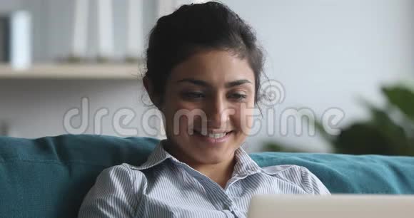 快乐的印度女人躺在沙发上在家里用电脑视频的预览图