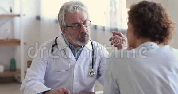 友好的老年男性医生穿白大褂咨询女性视频的预览图