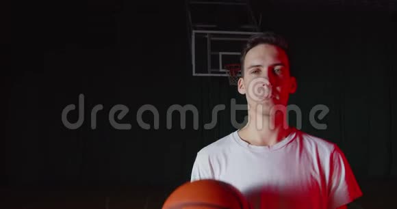 特写白种人青年篮球运动员肖像红光光束黑色暗篮背景视频的预览图