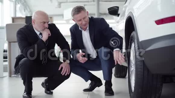 严肃的高加索人和新车旁边的汽车经销商坐在舱里交易员咨询客户视频的预览图