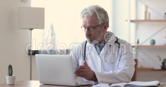 年纪较大的医生与病人交谈用手提电脑打视频电话视频的预览图