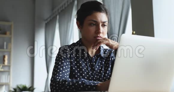 专注的印度年轻女性看着电脑显示器视频的预览图