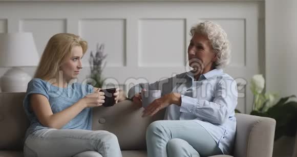 快乐的年轻女士坐在沙发上和年长的母亲聊天视频的预览图
