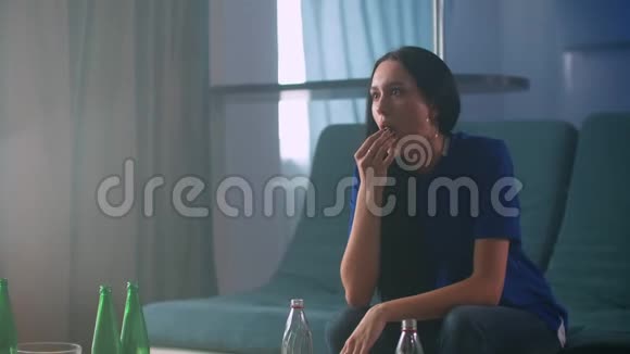 一张年轻貌美的女人坐在沙发上看着爆米花和啤酒的照片视频的预览图