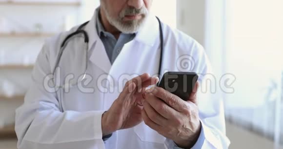 持有智能手机短信的高级男性医生关闭查看视频的预览图