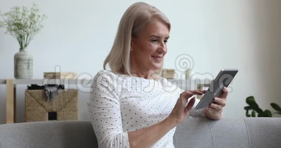 幸福中年奶奶用数码平板坐在沙发上视频的预览图