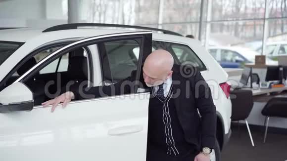 秃顶白种人高级男子站在旁边打开白色汽车在经销商和显示拇指成功视频的预览图