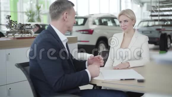 年轻微笑的白种人女人把名片递给汽车经销商的成年男子商人和客户握手视频的预览图
