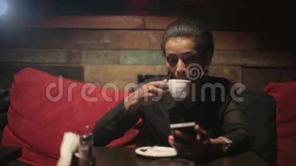 黑人妇女喝热咖啡使用智能手机视频的预览图