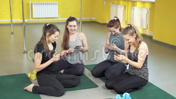 一群穿运动服的年轻女性积极使用手机四个女孩坐在垫子上完全专注于他们的智能手机视频的预览图