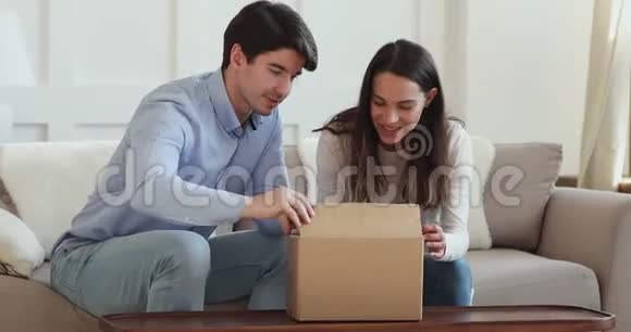 年轻夫妇兴奋地打开坐在沙发上的纸板箱视频的预览图