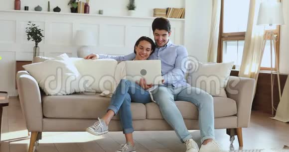 轻松的年轻夫妇在客厅沙发上使用笔记本电脑视频的预览图