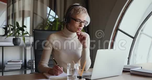 坐在办公桌旁戴着耳机的年轻女商人视频的预览图