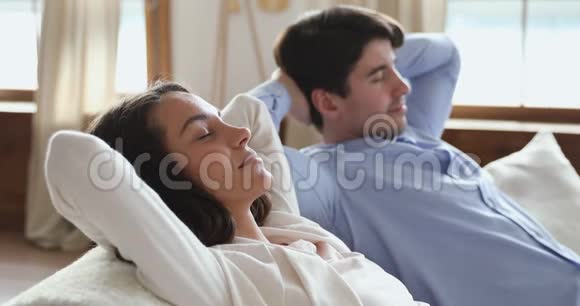 微笑安详的年轻夫妇闭上眼睛在沙发上放松视频的预览图