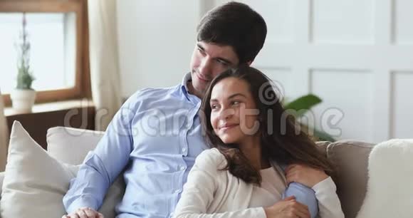 幸福的年轻夫妇拥抱在沙发上梦想着家庭目标视频的预览图