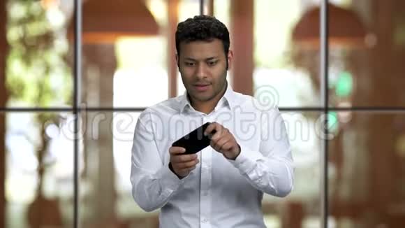 兴奋的深色皮肤的家伙在他的智能手机上玩游戏视频的预览图