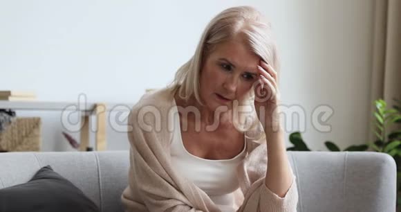 沮丧成熟的老女性退休者坐在沙发上感到焦虑视频的预览图