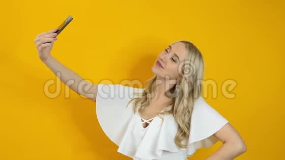 漂亮的金发女人在智能手机上自拍与黄色背景隔绝视频的预览图