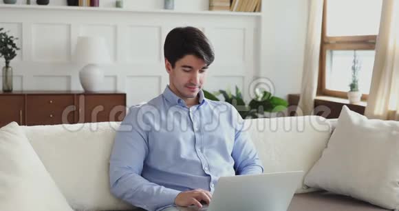 千禧一代用笔记本电脑坐在客厅的沙发上视频的预览图