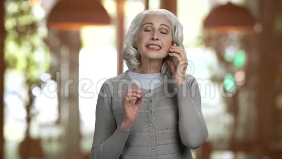 老灰头发的女士在电话里友好地交谈笑着视频的预览图