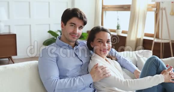 微笑的年轻夫妇坐在沙发上看着摄像机视频的预览图