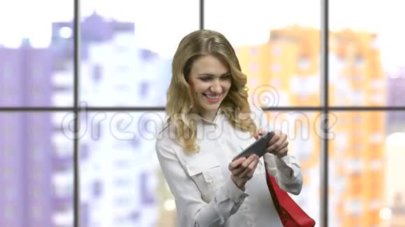 兴奋的年轻女孩穿着正式的衬衫在她的智能手机上玩游戏视频的预览图