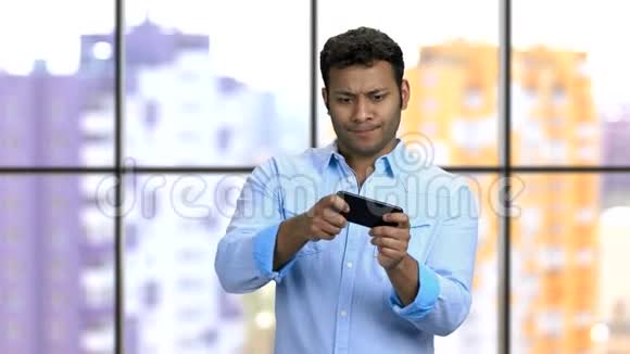 富有表现力的年轻深色皮肤男人玩智能手机游戏视频的预览图