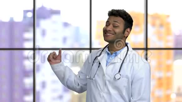 年轻的深色皮肤的印度教医生旋转着用拇指指向后面视频的预览图