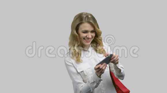年轻迷人的女人穿着正式的衬衫在她的智能手机上玩游戏视频的预览图