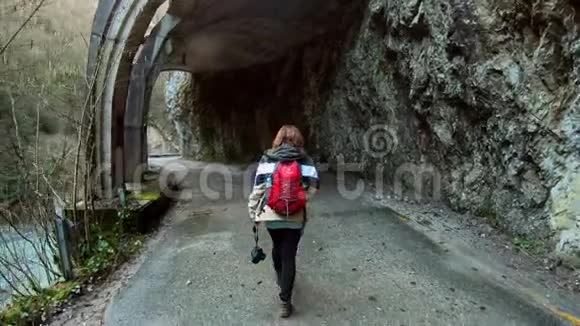 一位年轻的女摄影师背着背包沿着一条美丽的山路旅行视频的预览图