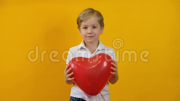 有趣的快乐小男孩蹒跚学步手里拿着红色心形气球在黄色的背景上微笑视频的预览图