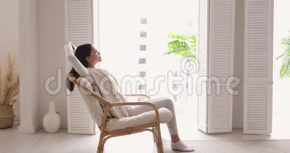 快乐的单身年轻女子坐在舒适的扶手椅上伸展视频的预览图