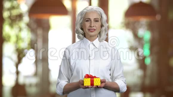 老太太穿着白色衬衫双手拿着礼品盒视频的预览图