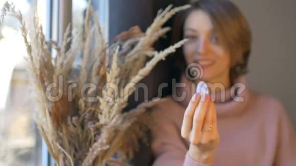 女人拿着透明紫罗兰紫水晶石做成的玉尼蛋站在窗户附近放着一瓶小穗子视频的预览图