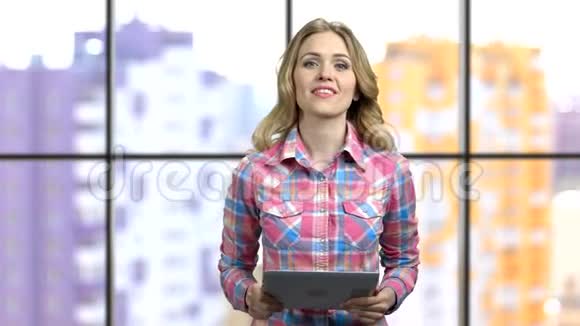 年轻快乐的女孩穿着格子衬衫拿着平板电脑演讲视频的预览图