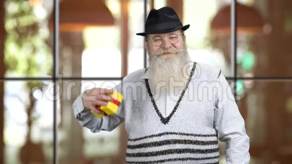 老退休爷爷用红色丝带指着黄色的礼盒视频的预览图