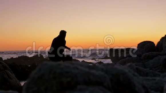 在太平洋海岸看日落的岩石上放松的男人视频的预览图