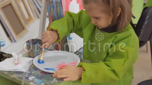 一个小女孩在艺术工作室里坐在画架上画纸视频的预览图