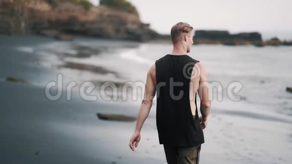 一个高个子男人沿着海滩走火山沙和海洋视频的预览图
