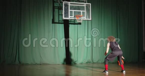 篮球运动员卷曲地看着篮筐抱着球准备自信独自阴影明亮的光束训练比赛视频的预览图