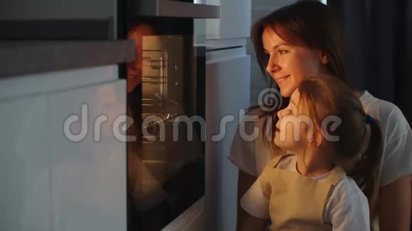 母亲和女儿在烤箱里看着馅饼快乐的童年一起做自制披萨视频的预览图