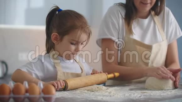 妈妈帮女儿在厨房里卷面团来烤饼干妈妈和女儿一起在厨房里烤披萨女孩视频的预览图