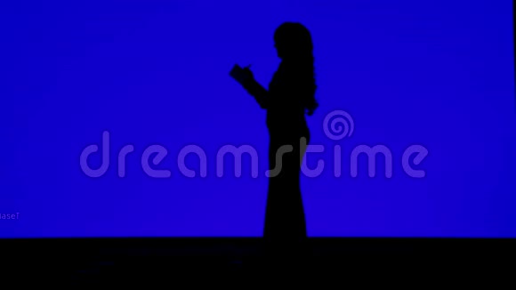 一个身材苗条的女人的剪影卷发在蓝色背景上的笔记本上素描视频的预览图