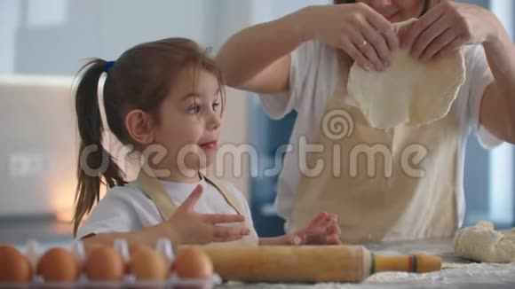 中镜头的母亲和女儿滚动面团在厨房妈妈教女儿做面团女孩学做饭视频的预览图