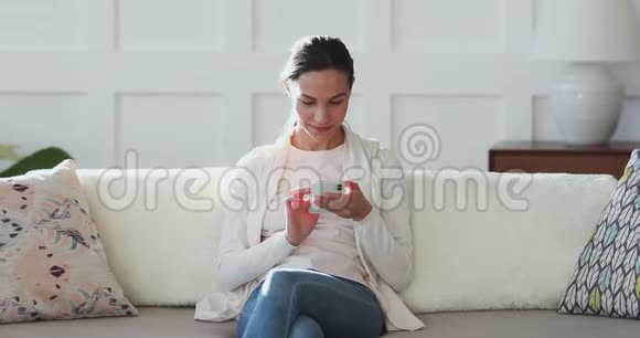 在舒适的公寓里使用手机的快乐千禧女性视频的预览图