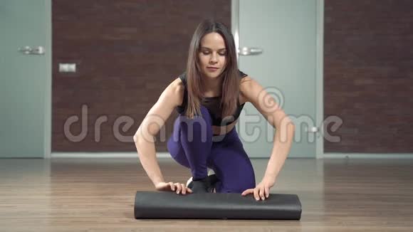 准备瑜伽课的过程年轻快乐的女人在家里或工作室锻炼前滚动垫子视频的预览图