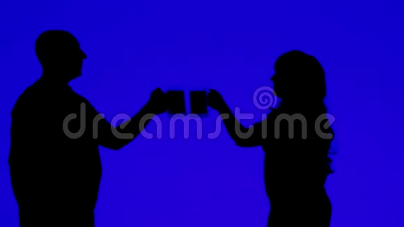 一个女人和一个男人用蓝色背景的杯子喝啤酒的剪影视频的预览图